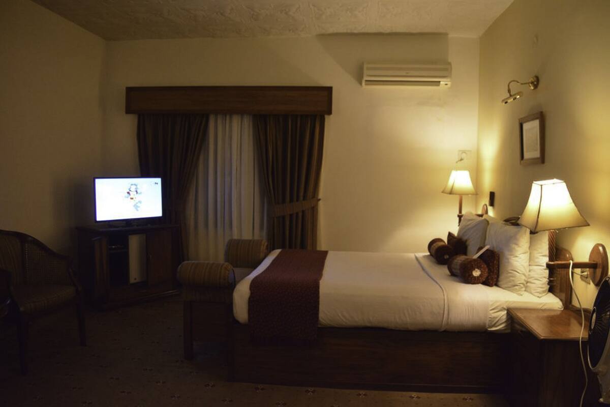 A hotel room with a bed, a television, a desk, a chair, and two lamps.