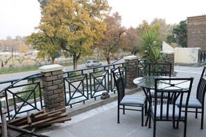An outdoor patio with a glass table and chairs, stone pillars, and a view of the street and trees. - Chateau Royal (Islamabad)