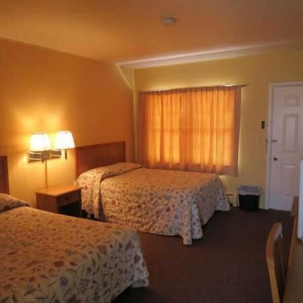 Une chambre d’hôtel avec deux lits, une table de chevet, une lampe, une fenêtre avec des rideaux et une porte.