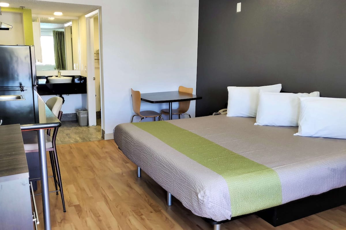 A hotel room with a bed, a desk, a chair, a small table, and a mirror.