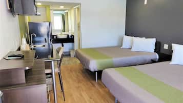 A compact hotel room with a kitchenette, two single beds, a desk with a chair, and a TV.