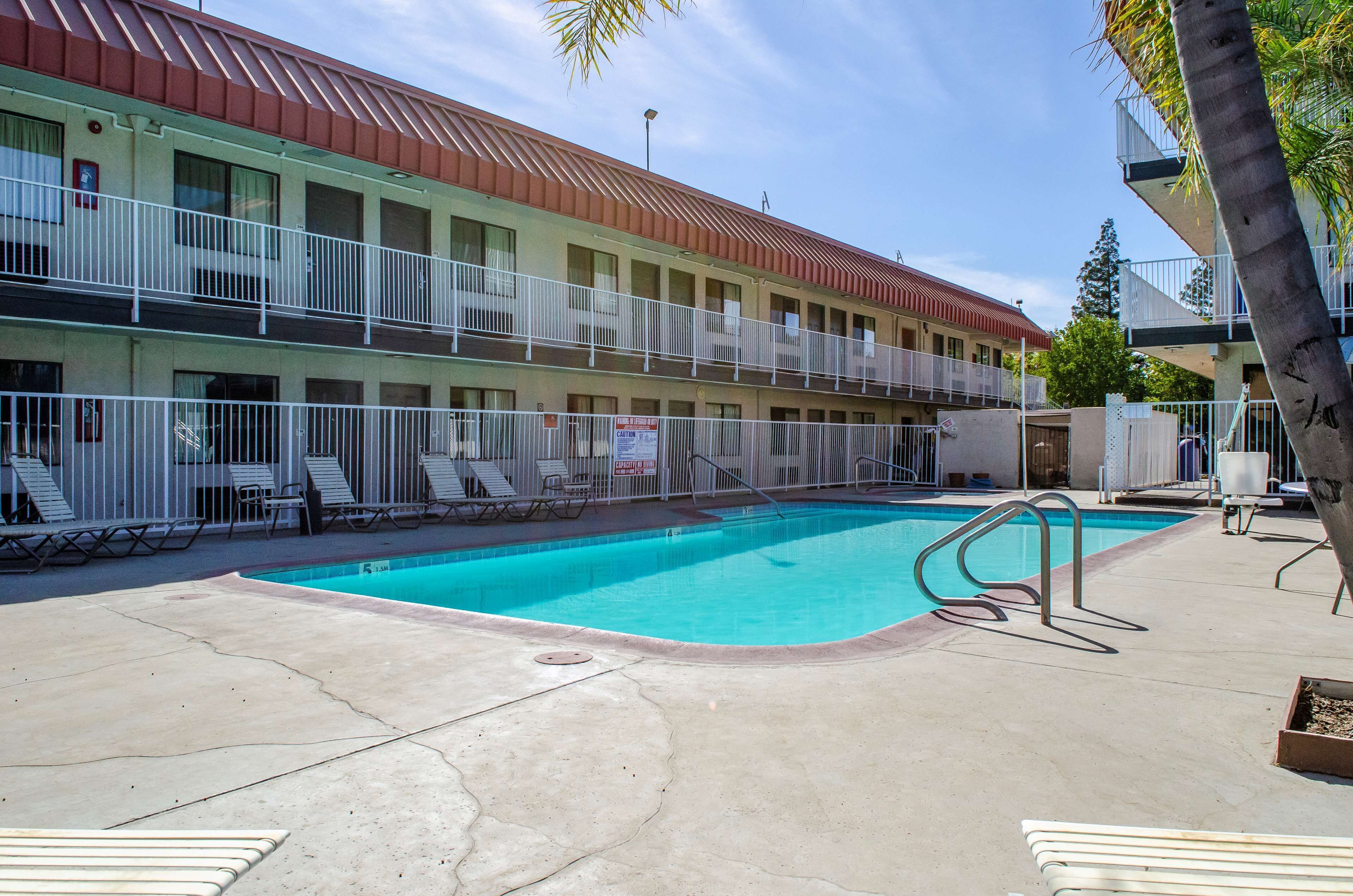A motel with a swimming pool, multiple balconies, and lounge chairs.