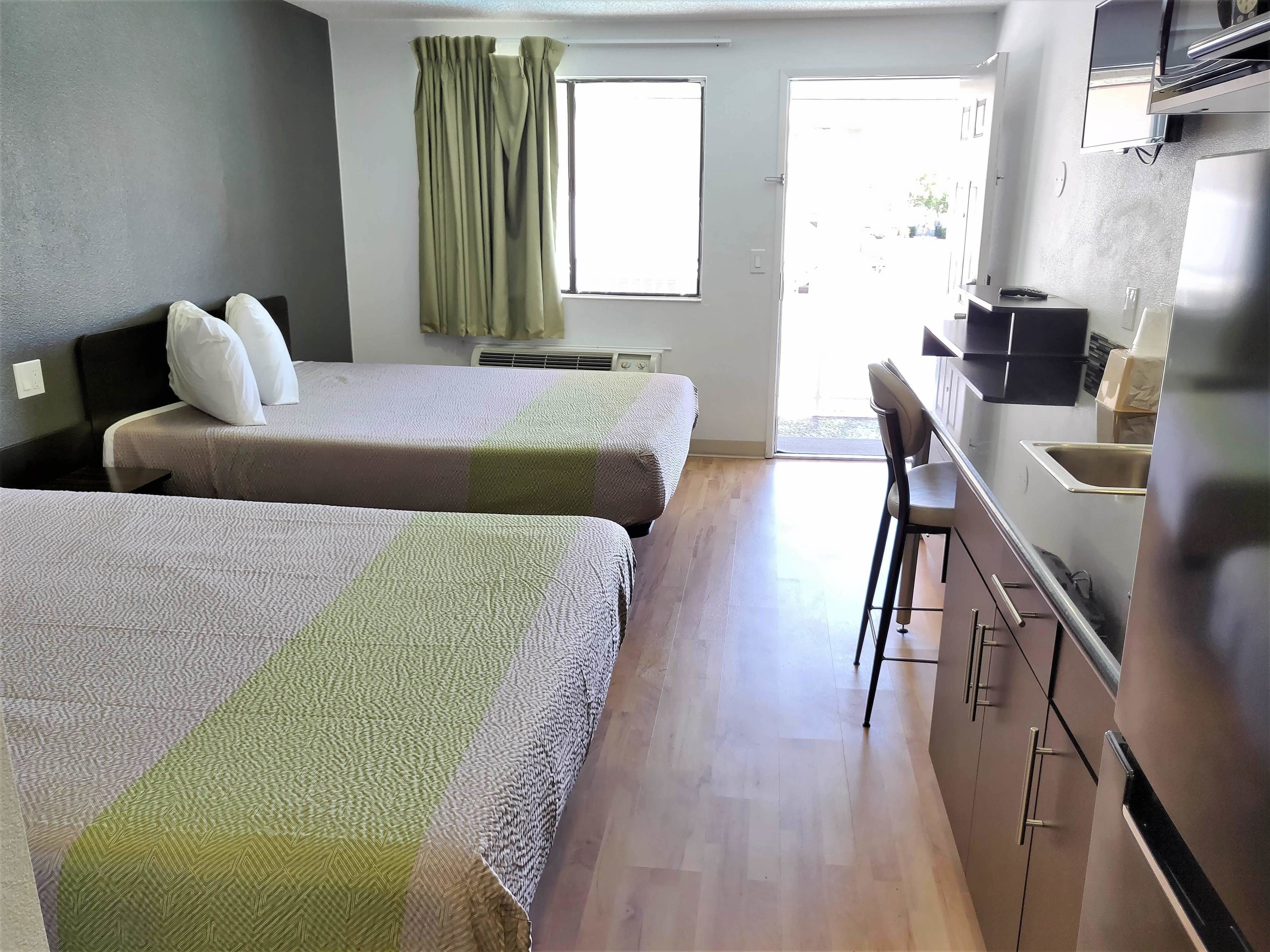 A hotel room with two beds, a desk, a chair, a TV, and a kitchenette.