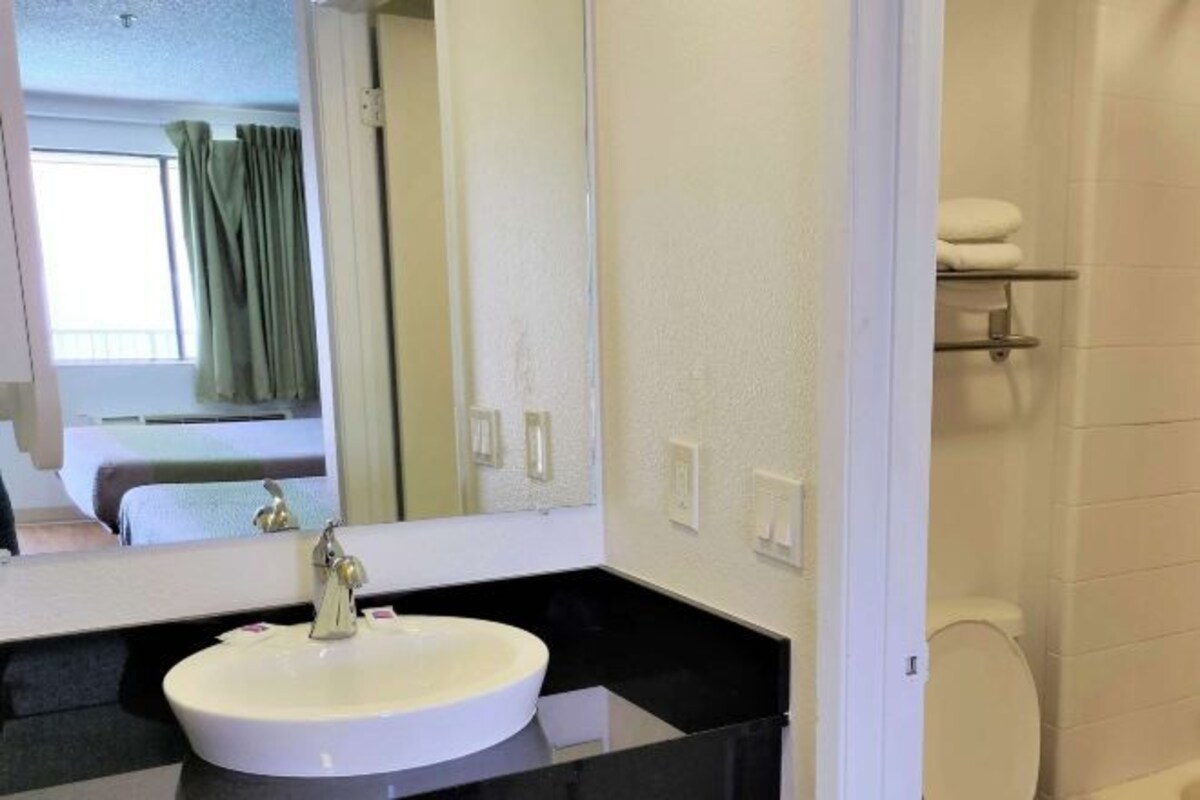 A hotel bathroom with a white sink, a large mirror, and a toilet.