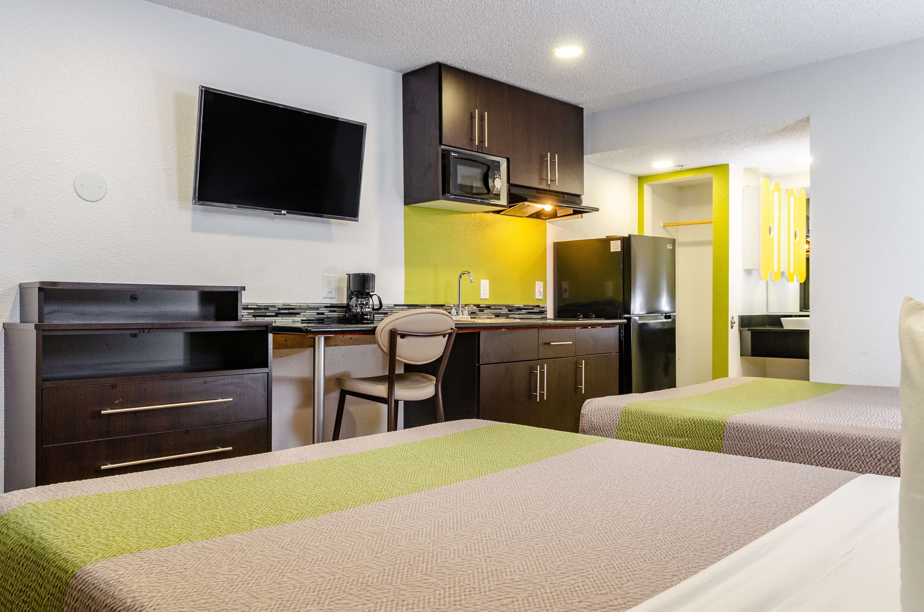 Habitación de hotel con cama, escritorio y silla, televisor, microondas, refrigerador y una pequeña cocina.