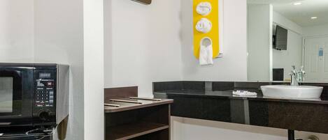 A modern bathroom with a black countertop, white sink, and a microwave.