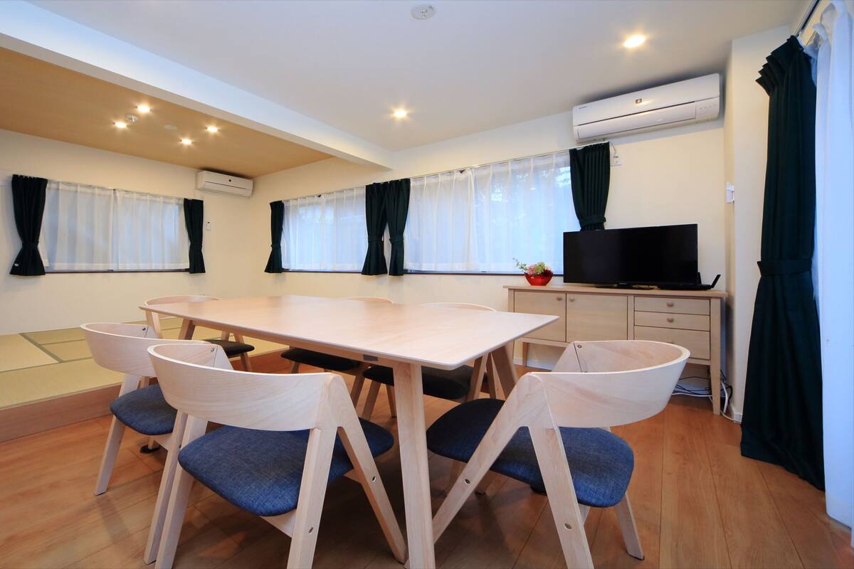 A room with a wooden table and chairs, a television, and an air conditioning unit.