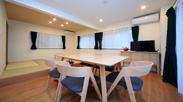 A room with a wooden table and chairs, a television, and an air conditioning unit. - COTO Tokyo Shibuya 4 (Tokyo)
