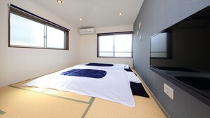 A room with two beds, large windows, an air conditioning unit, and a television. - COTO Tokyo Shibuya 4 (Tokyo)