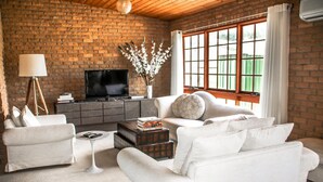 A living room with a brick wall, a television, a white sofa, a coffee table, and a window with curtains. - Brigham House (Tooma)
