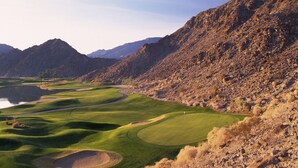 Un parcours de golf avec un obstacle d’eau, entouré d’un terrain rocheux et de montagnes.