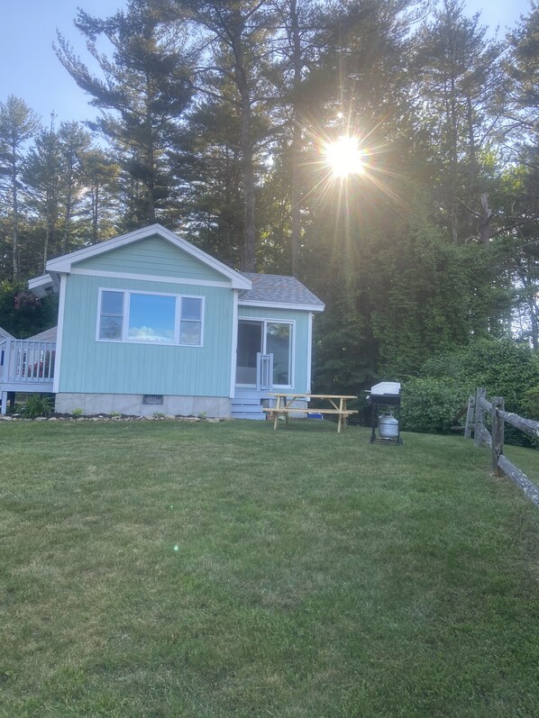 A small, light blue house with a front porch and a picnic table in a grassy yard.