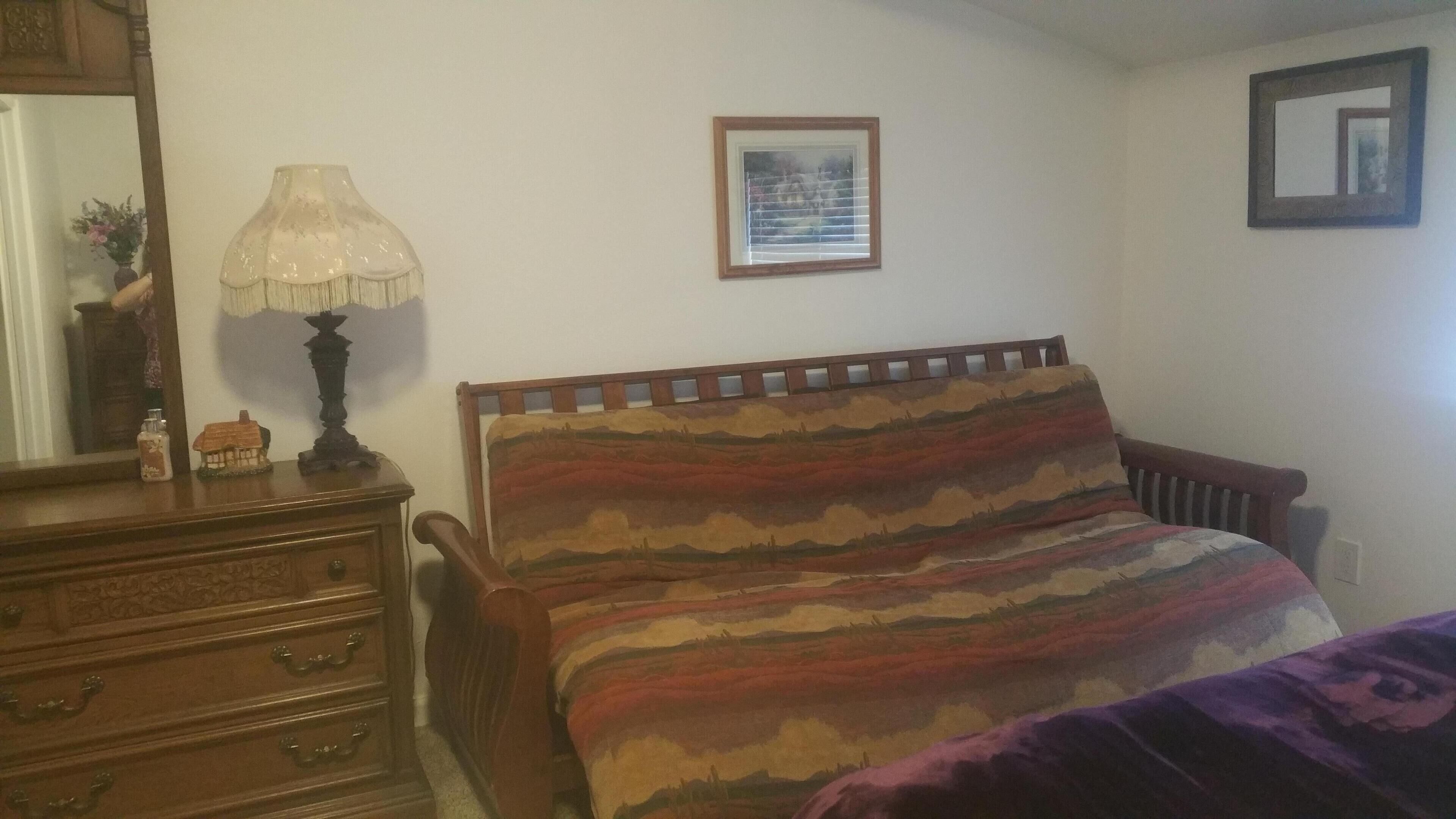 Une chambre à coucher avec un lit en bois, une commode, une lampe et un tableau encadré au mur.
