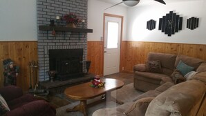 A living room with a fireplace, wooden walls, a brown sofa, and a coffee table.