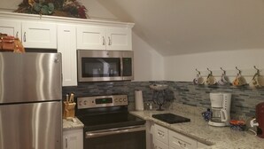 A kitchen with white cabinets, stainless steel appliances, a microwave, a coffee maker, and a hanging pot rack.