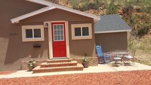 A small house with a red door, two windows, and a brick staircase leading to the entrance.