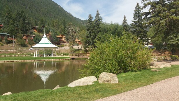 A tranquil lakeside scene with a gazebo, a wooden bridge, and a mountain backdrop.