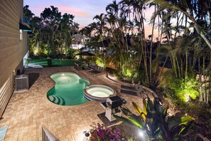 A backyard with a swimming pool, a hot tub, and a barbecue area surrounded by palm trees and plants. - Casa Leone | Heated Pool & Spa, Pet Friendly, Putting Green (Siesta Key)