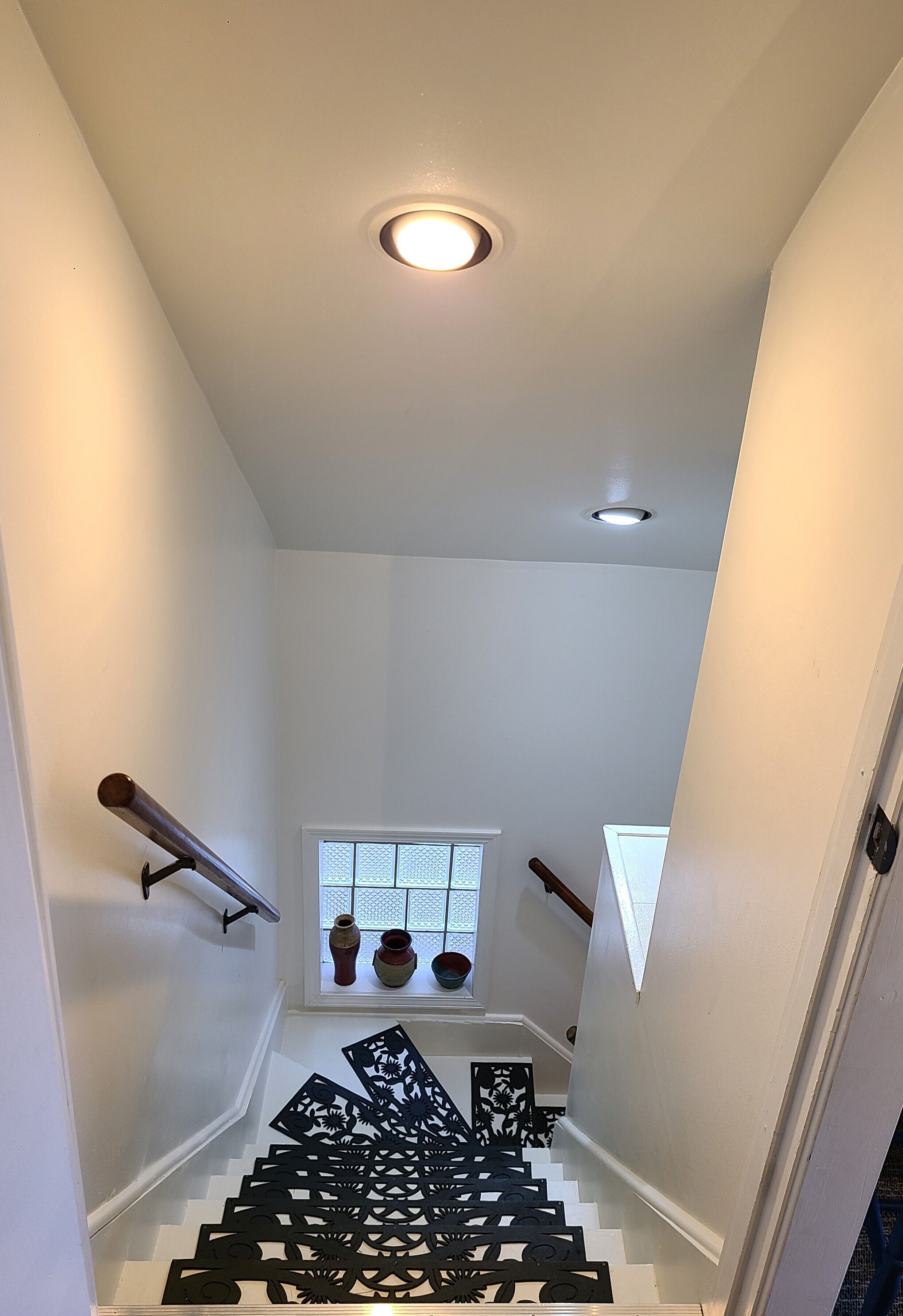 Una escalera con un corredor estampado, una ventana con jarrones decorativos y una lámpara de techo.