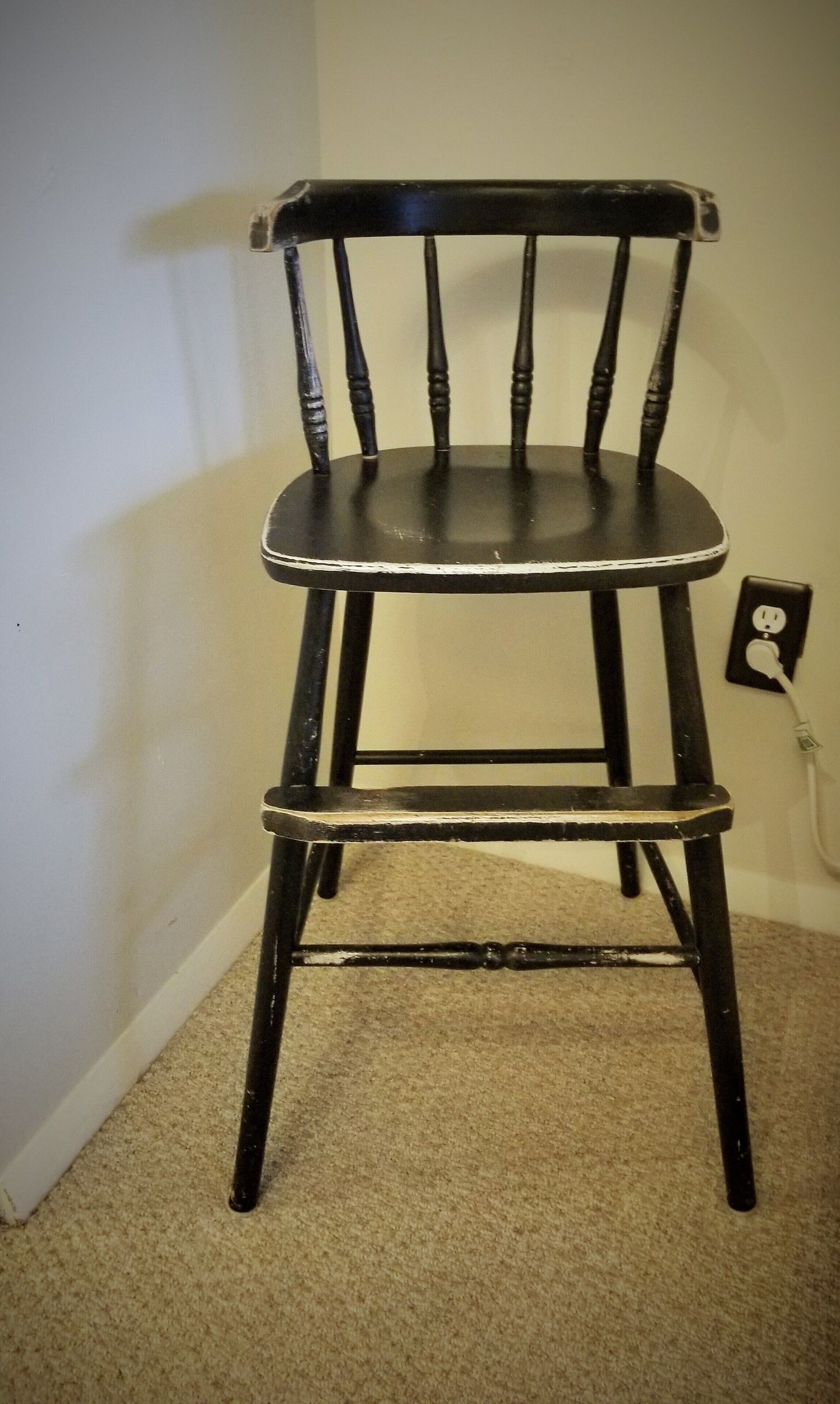 Una silla de madera con respaldo alto y asiento, ubicada frente a una pared con un enchufe cerca.