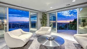 Ein modernes Wohnzimmer mit Panoramablick auf die Stadt, zwei weiße Sofas, ein runder Couchtisch und eine große Glasdoor.