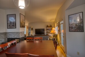 A dining area with a large wooden table and chairs, a flat-screen TV, and a fireplace.