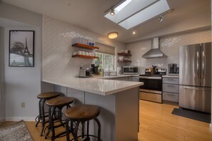 A modern kitchen with a large island, bar stools, stainless steel appliances, and a herringbone tile backsplash.