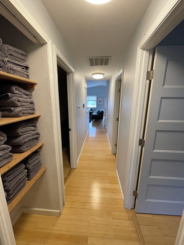 A hallway with wooden floors, a blue door, and shelves with folded towels.