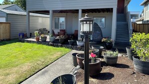 A modern house with a covered patio area, outdoor seating, and potted plants. -  N TacomaPt Ruston 2bd. 2bath retreat w/ EV charger, A/C & relaxing water views (Tacoma)