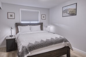 A bedroom with a bed, bedside tables, a window with blinds, and framed pictures on the wall.