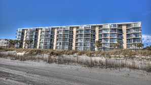 Un hotel de varios pisos con balcones, situado cerca de una playa de arena.