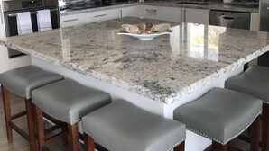 Eine moderne Küche mit Granit Arbeitsplatten, Edelstahlgeräten und einer zentralen Kochinsel mit Barhocker.