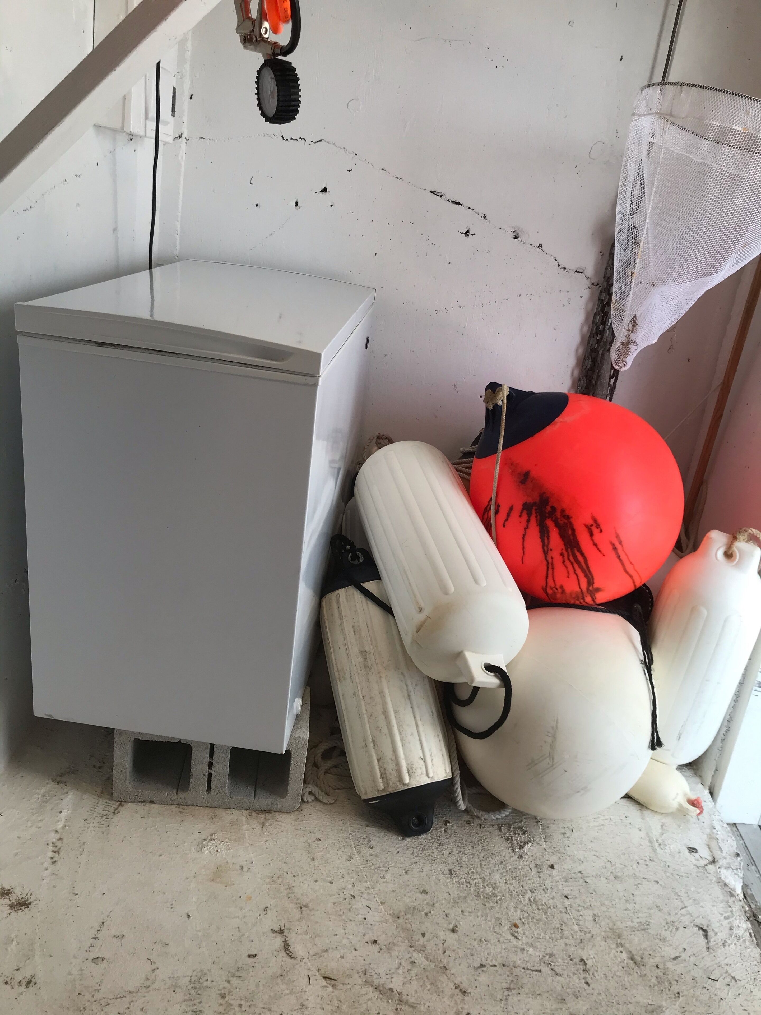 Eine Raumecke mit einer weißen Wand, einem grauen Schrank und einem weißen Kunststoffbehälter mit einer Kordel.
