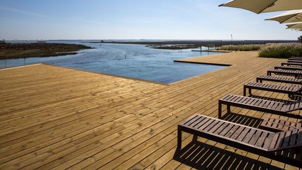 Une terrasse en bois, dotée de chaises longues et de parasols, qui offre une vue sur une étendue d’eau calme.