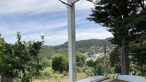 Una mesa de madera con una silla blanca, ubicada al aire libre con vistas a un pueblo y colinas al fondo.