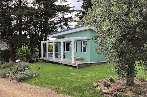 Une petite maison de plain-pied, dotée d’un porche et d’une terrasse, entourée d’un jardin bien entretenu et d’arbres.