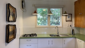 Una cocina con gabinetes blancos, estufa a gas, lavamanos y dos lámparas colgantes.