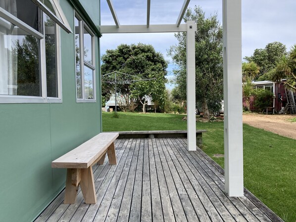 Una terraza de madera con un banco, un pérgola y vistas a un césped verde y árboles.