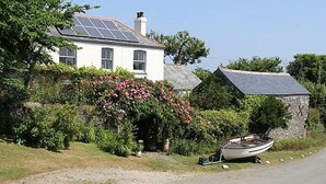 A white house with solar panels, a boat, and lush greenery.