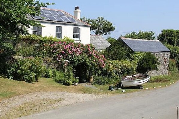 A white house with solar panels, a boat, and lush greenery.