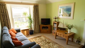 A living room with a sofa, a television, a bookshelf, a table, and a window with curtains.