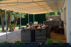 Un patio al aire libre con una zona de estar cubierta, una mesa lista para comer y plantas en macetas.