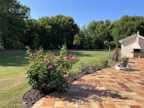 A patio area with a brick floor, a garden with pink flowers, and a barbecue area with a chimney.