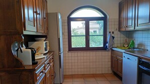 Una cocina con armarios de madera, un refrigerador, un microondas y una ventana con vista a la vegetación.