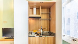 Une cuisine compacte équipée d’un four encastré, d’un évier et d’une fenêtre donnant sur un immeuble.