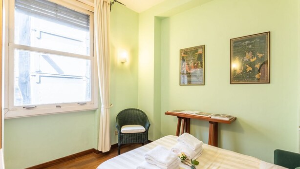 Une pièce comprenant un lit, une chaise, une table avec des livres et deux tableaux encadrés accrochés au mur.