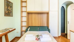 Une chambre à coucher avec un lit, une armoire en bois, une petite table avec des livres et un tableau encadré au mur.