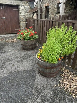 A stone building with a wooden door and a wooden fence. There are two large flower pots with plants and flowers. - Grooms Cottage- Sleeps 4 in 2 bedrooms plus 2 to 4 dogs depending on size. (Bodmin)