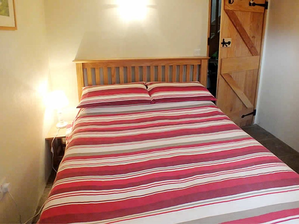 Un lit avec une couvre-lit à rayures, une tête de lit en bois et une table de chevet avec une lampe.