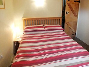 Ein Bett mit gestreiftem Bettbezug, einem Holz-Kopfteil und einem Nachttisch mit Lampe.